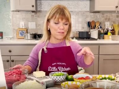 Amy Roloff is wearing a pink apron that says Amy Roloff's Little Kitchen on it.